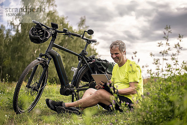 Reifer Mann benutzt digitales Tablett während seiner Fahrradtour mit einem E-Bike