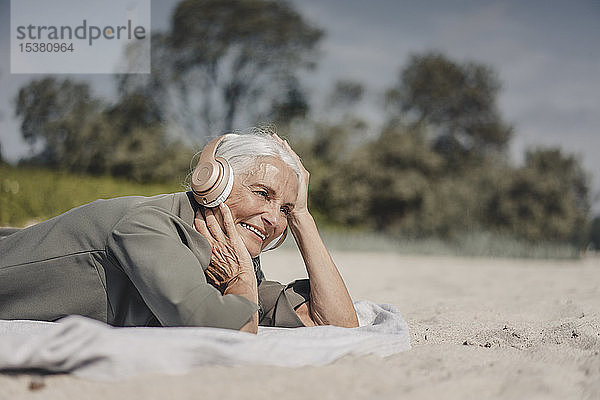Ältere Frau  die am Strand mit Kopfhörern Musik hört