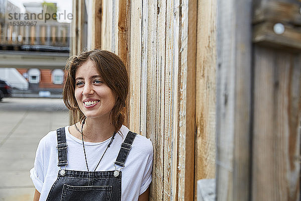 Porträt einer lächelnden jungen Frau  die sich an einen Holzzaun lehnt