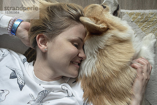 Glückliche Frau liegt zu Hause auf dem Blumenbeet und kuschelt mit ihrem Hund
