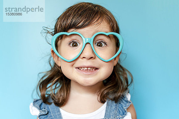 Bildnis eines süßen kleinen Mädchens mit herzförmiger Brille auf blauem Hintergrund
