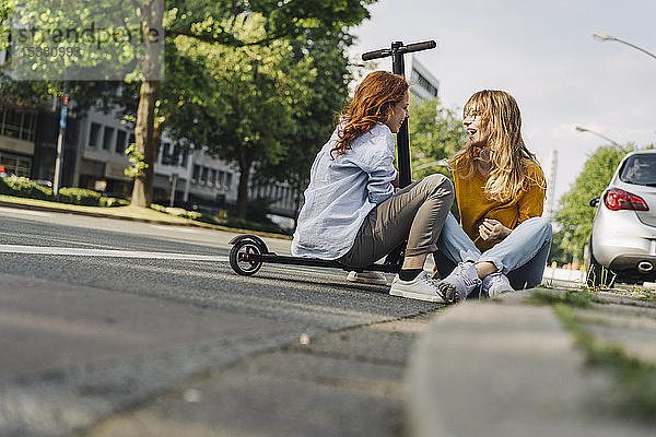 Freundinnen mit E-Scooter im Gespräch am Straßenrand in der Stadt