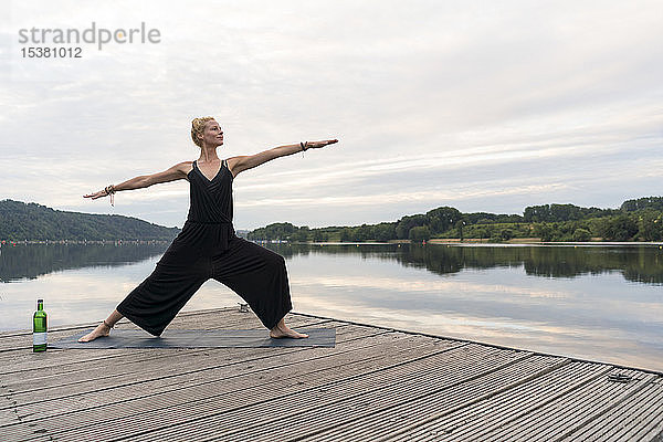Junge Frau  die auf einem Steg an einem See Yoga praktiziert