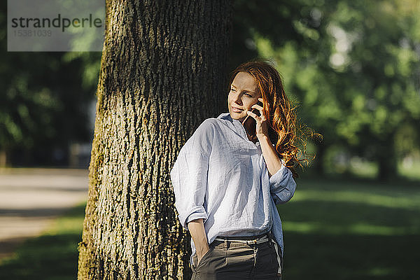 Rothaarige Frau telefoniert im Park