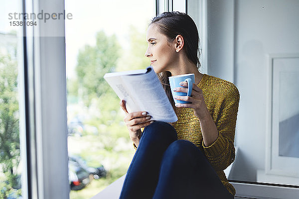 Junge Frau schaut aus dem Fenster  während sie zu Hause ein Buch liest