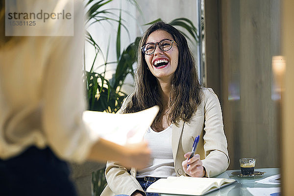 Lachende Geschäftsfrau sieht Kollegin im modernen Büro an