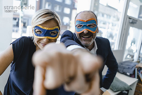 Geschäftsmann und -frau mit Superhelden-Masken  die auf die Kamera zeigen