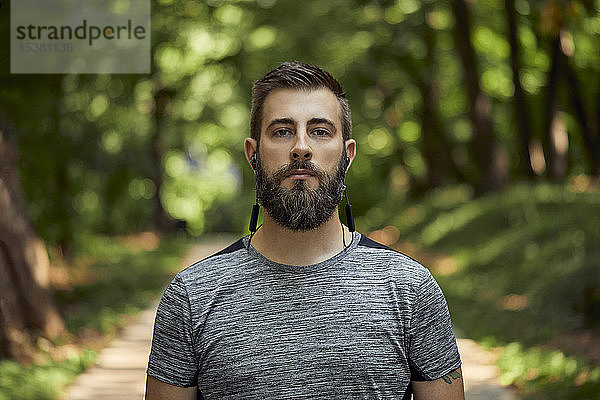 Porträt eines sportlichen Mannes mit Kopfhörern im Wald