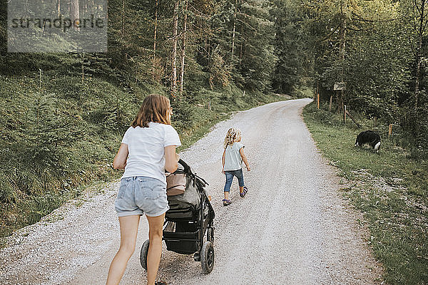 Mutter mit Tochter  Kinderwagen und Hund auf Waldweg