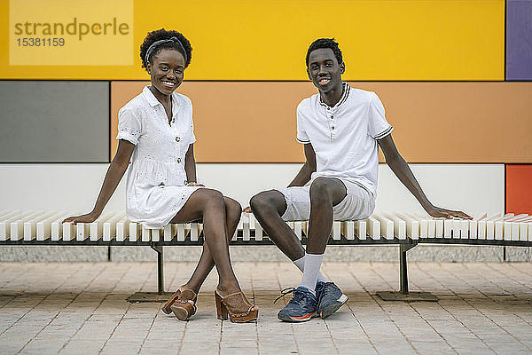 Porträt eines glücklichen jungen Paares auf einer Bank im Freien sitzend