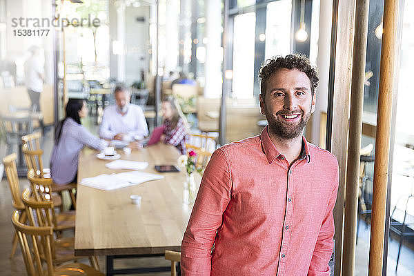 Porträt eines Gelegenheits-Geschäftsmannes in einem Cafe mit Kollegen  die im Hintergrund ein Treffen haben