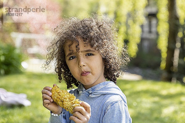 Porträt eines Jungen  der im Garten einen Maiskolben isst