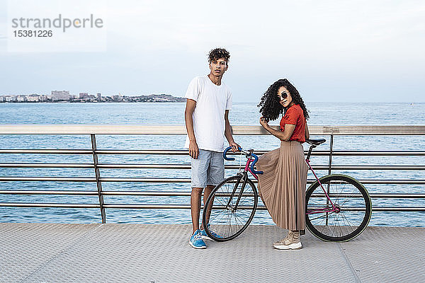 Junges Paar mit Fahrrad  stehend auf einer Brücke am Meer