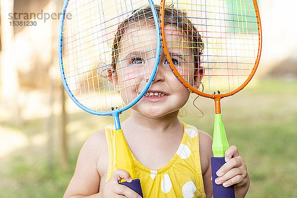 Kleines Mädchen spielt im Sommer mit bunten Badmintonschlägern im Freien