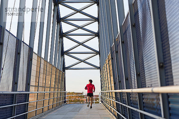 Rückansicht eines auf einer Brücke laufenden Joggers mit Smartphone in der Armtasche