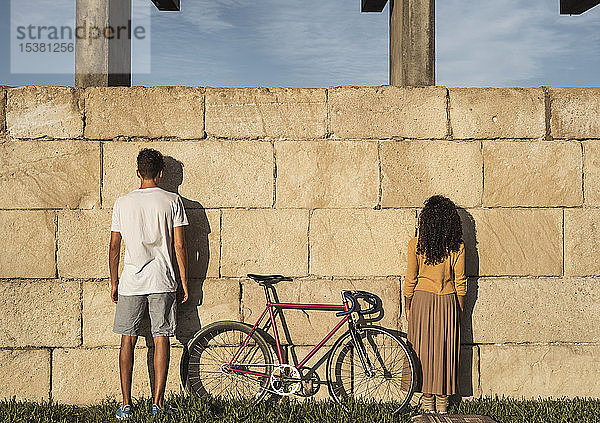 Junges Paar mit Fahrrad  vor der Wand stehend  Rückansicht