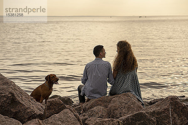 Junges Paar mit Hund abends am Strand