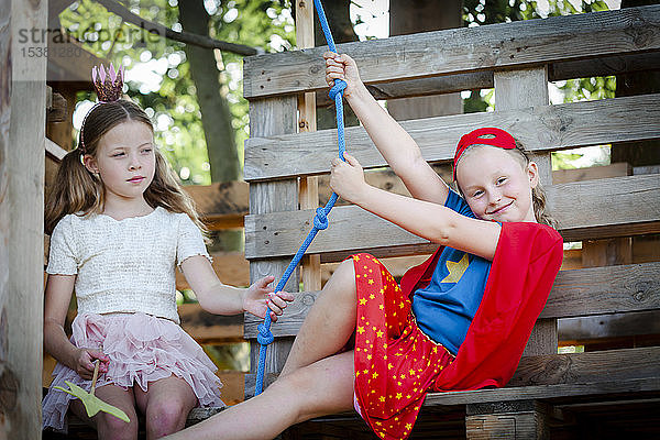 Als Prinzessin und Superwoman verkleidete Mädchen spielen in einem Baumhaus