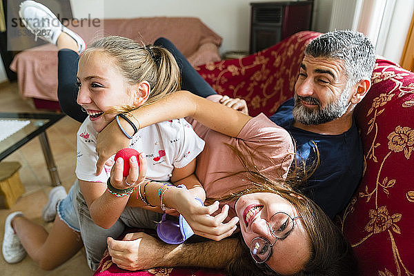 Vater mit zwei verspielten Töchtern auf der Couch zu Hause