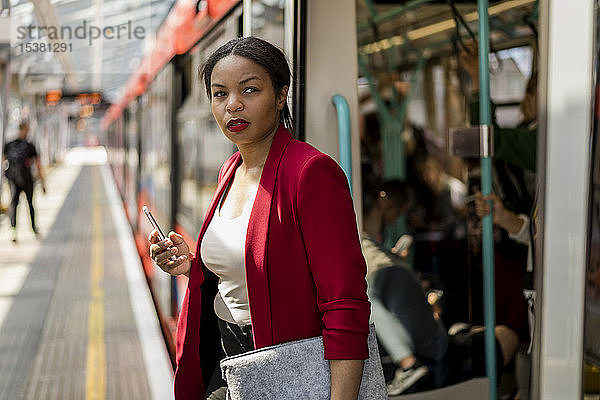 Porträt einer Geschäftsfrau mit Handy beim Aussteigen aus dem Zug  London  Großbritannien
