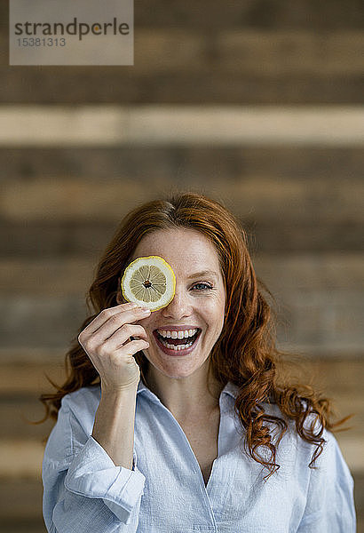 Porträt einer lachenden rothaarigen Frau  die das Auge mit einer Zitronenscheibe bedeckt