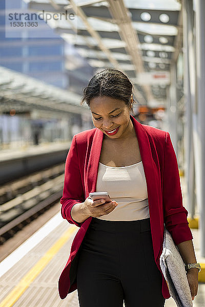 Lächelnde Geschäftsfrau auf der Plattform schaut auf Handy  London  UK