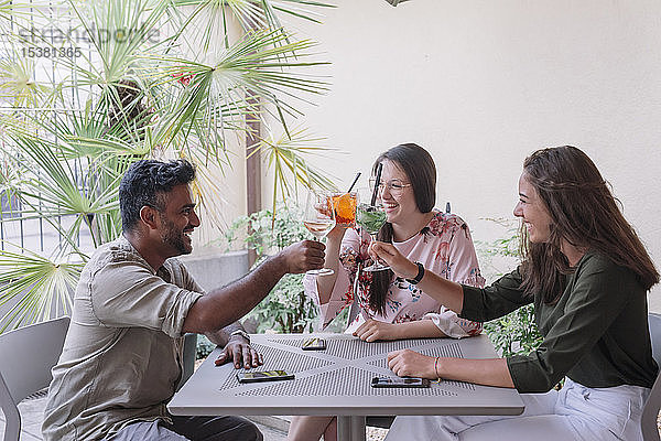 Glückliche Freunde sitzen am Tisch und stoßen an