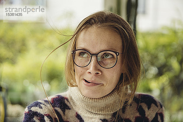 Porträt einer jungen Frau mit Brille  die einen flauschigen Pullover trägt  der eine Haarsträhne aufbläst