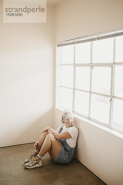 Lächelnde junge Frau  die in einem Raum auf dem Boden sitzt
