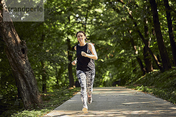 Sportliche junge Frau rennt auf Waldweg