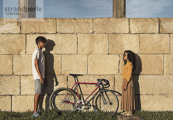 Junges Paar mit Fahrrad  vor der Wand stehend  von Angesicht zu Angesicht