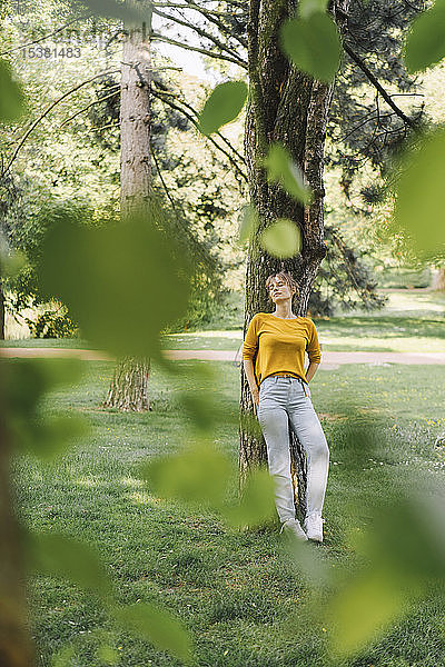 Junge Frau  die sich im Park an einen Baum lehnt
