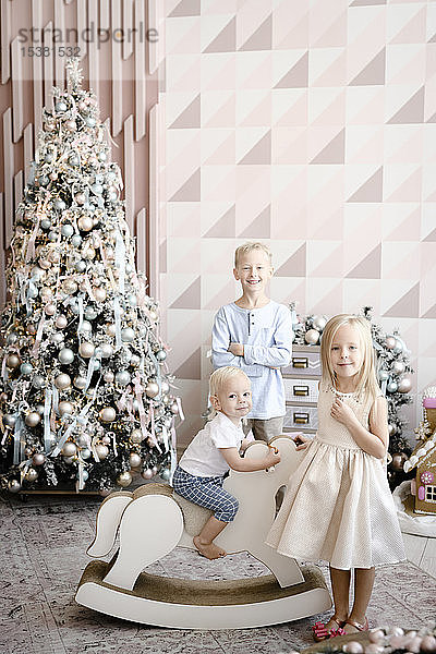 Gruppenbild von drei Kindern vor dem Weihnachtsbaum