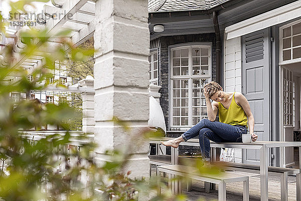 Entspannte Frau sitzt auf dem Terrassentisch im Garten ihres Hauses