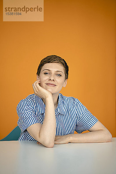 Porträt einer auf Tisch gelehnten Frau mit orangem Hintergrund
