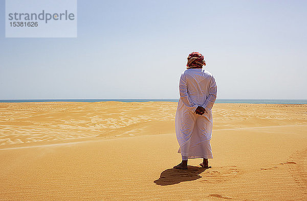 Beduine in Nationaltracht in der Wüste stehend  Rückansicht  Wahiba Sands  Oman