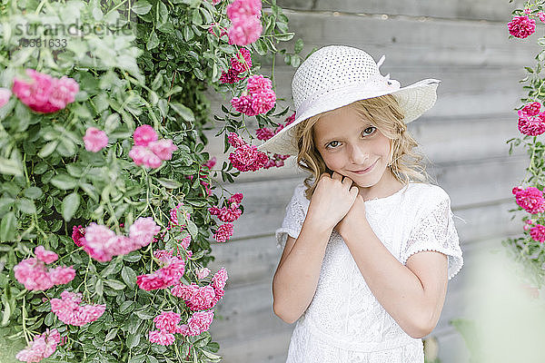 Porträt eines lächelnden Mädchens am Rosenbusch