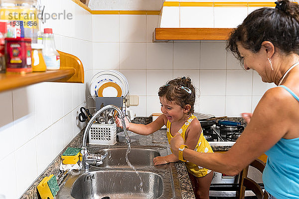 Kleines Mädchen und Großmutter spielen in der Küche mit Wasser