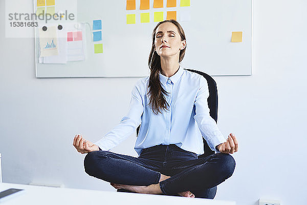 Junge Geschäftsfrau sitzt auf Bürostuhl und meditiert