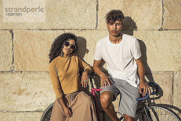 Junges Paar mit Fahrrad  an Steinmauer gelehnt  sieht cool aus