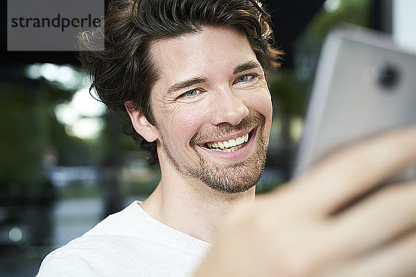 Porträt eines glücklichen Mannes mit Handy in der Hand in der Stadt