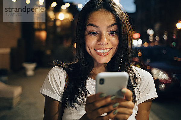 Junge Frau benutzt nachts in der Stadt ein Smartphone