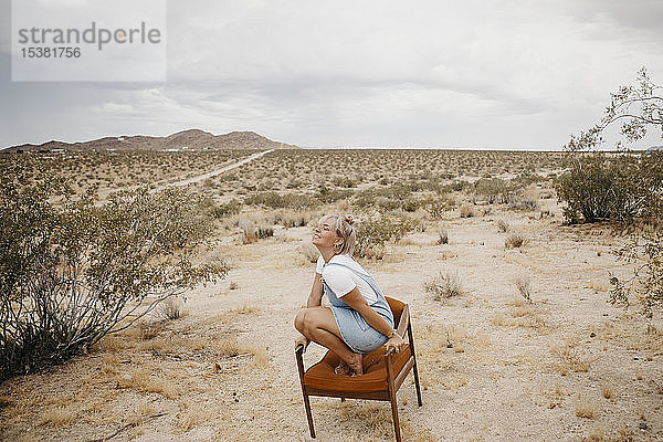 Auf einem Stuhl kauernde Frau in Wüstenlandschaft  Joshua-Tree-Nationalpark  Kalifornien  USA