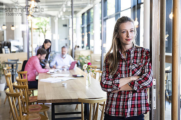 Porträt einer ungezwungenen Geschäftsfrau in einem Cafe mit Kollegen  die im Hintergrund eine Besprechung abhalten