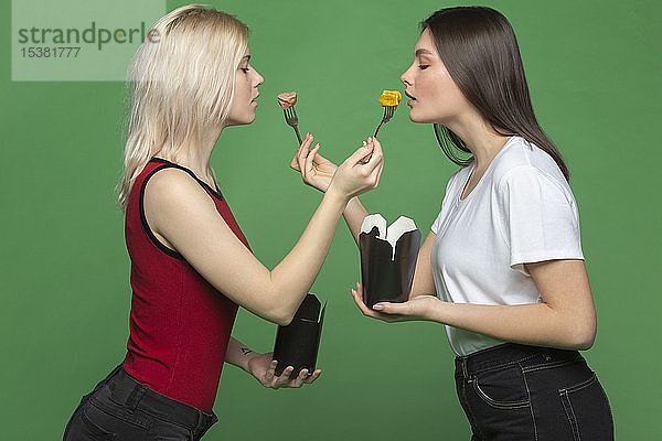 Zwei junge Frauen füttern sich gegenseitig vor grünem Hintergrund
