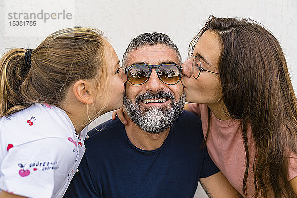 Zwei Töchter küssen glücklichen Vater