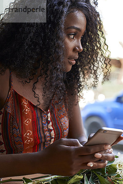 Porträt einer jungen afrikanischen Frau in einem Café  die ihr Smartphone überprüft
