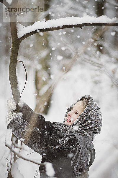 Porträt eines lächelnden kleinen Mädchens  das einen Baum im Winterwald schüttelt