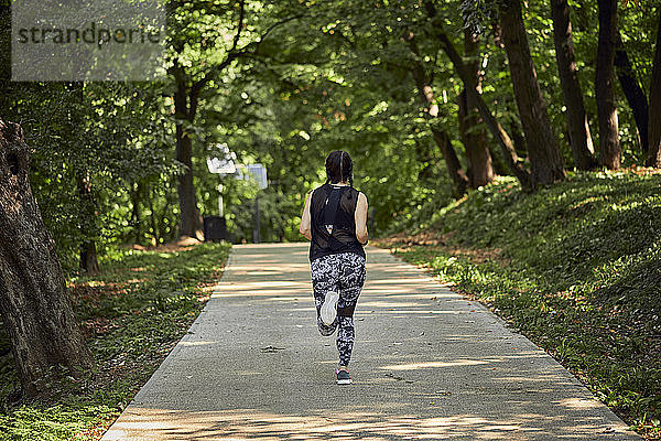 Rückansicht einer sportlichen jungen Frau  die auf einem Waldweg läuft