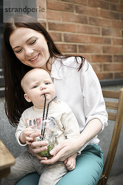 Lächelnde Mutter mit ihrem Limonade trinkenden Säugling